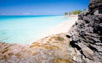 a beach with clear blue water and rocky cliffs